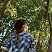 Young adult woman looking up at trees.
