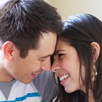 A young couple sitting close, looking at each other and smiling.