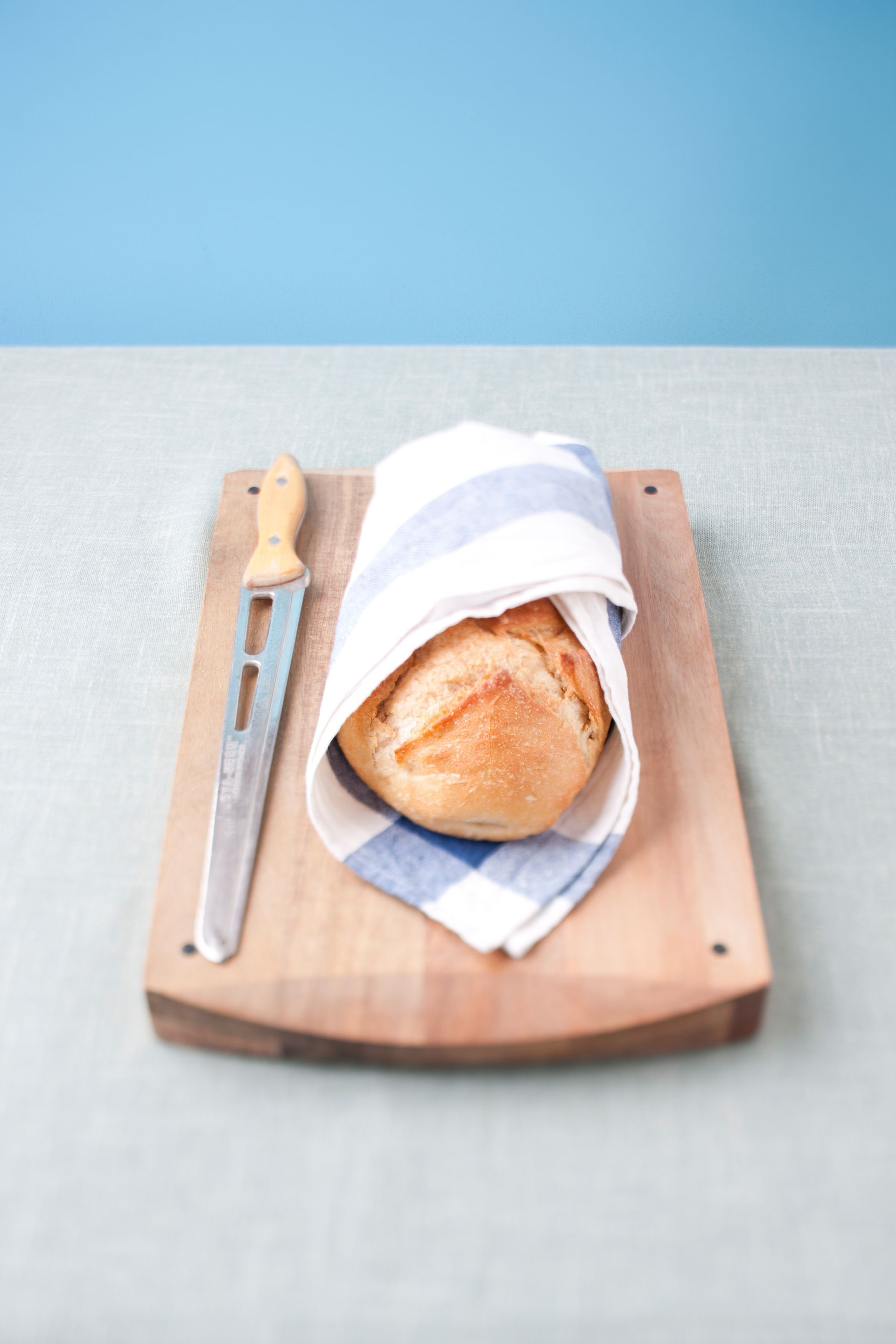 A loaf of bread wrapped in a towel on a cutting board.