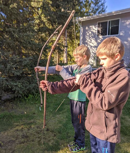 Two young brothers out in their back yard playing with Bows and Arrows.