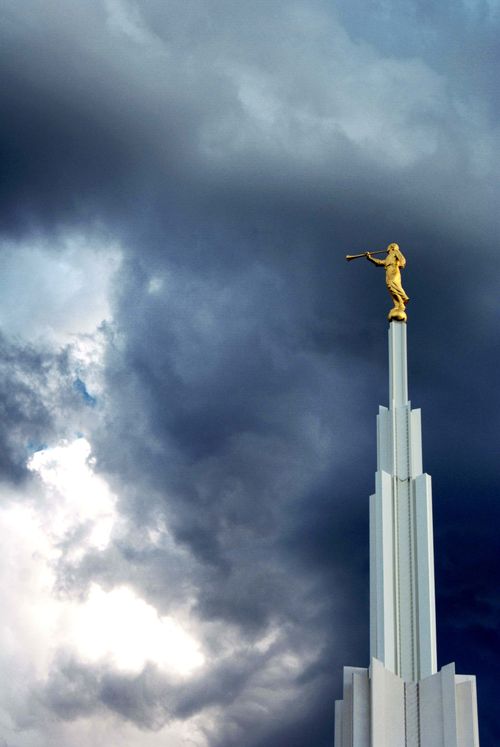 The spire and angel Moroni on top of the Denver Colorado Temple, with dark clouds in the background.