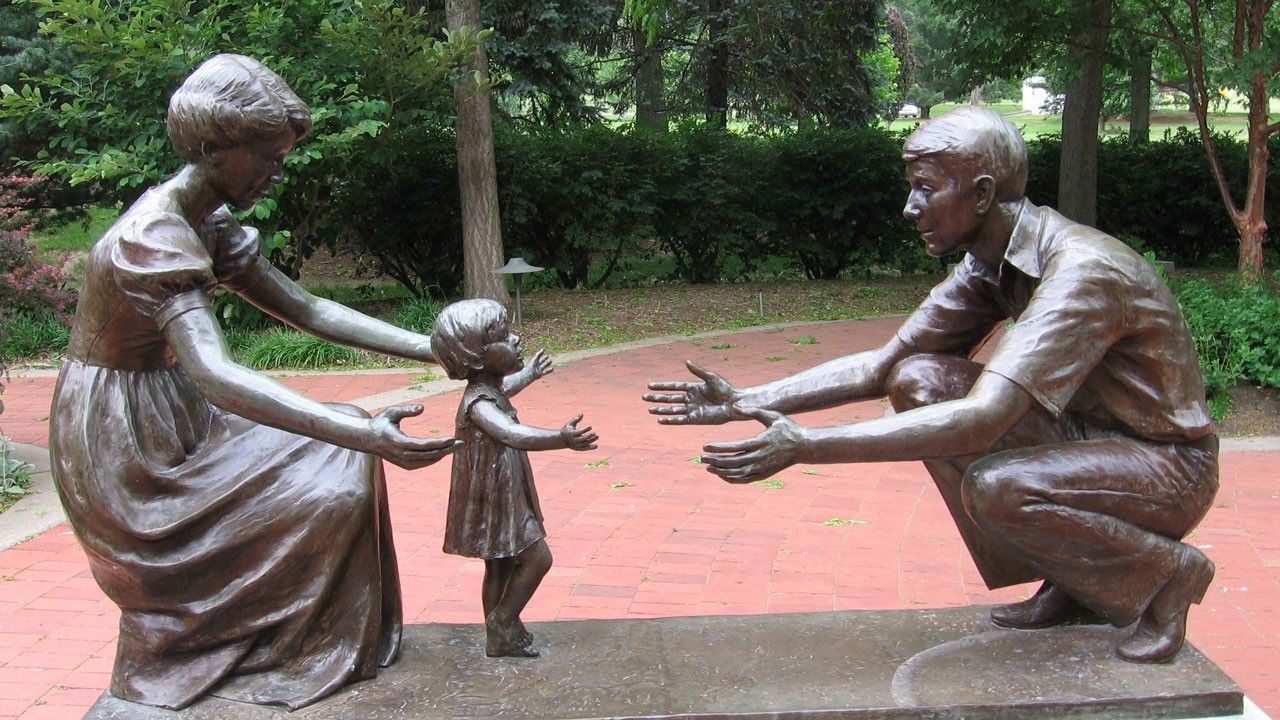 A bronze statue of a woman, man, and child. The scene symbolizes a child taking its first step.