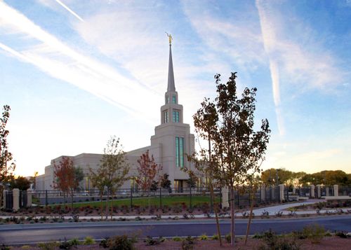 The Gila Valley Arizona Temple in the evening, with the fence surrounding the grounds, trees, and bushes.