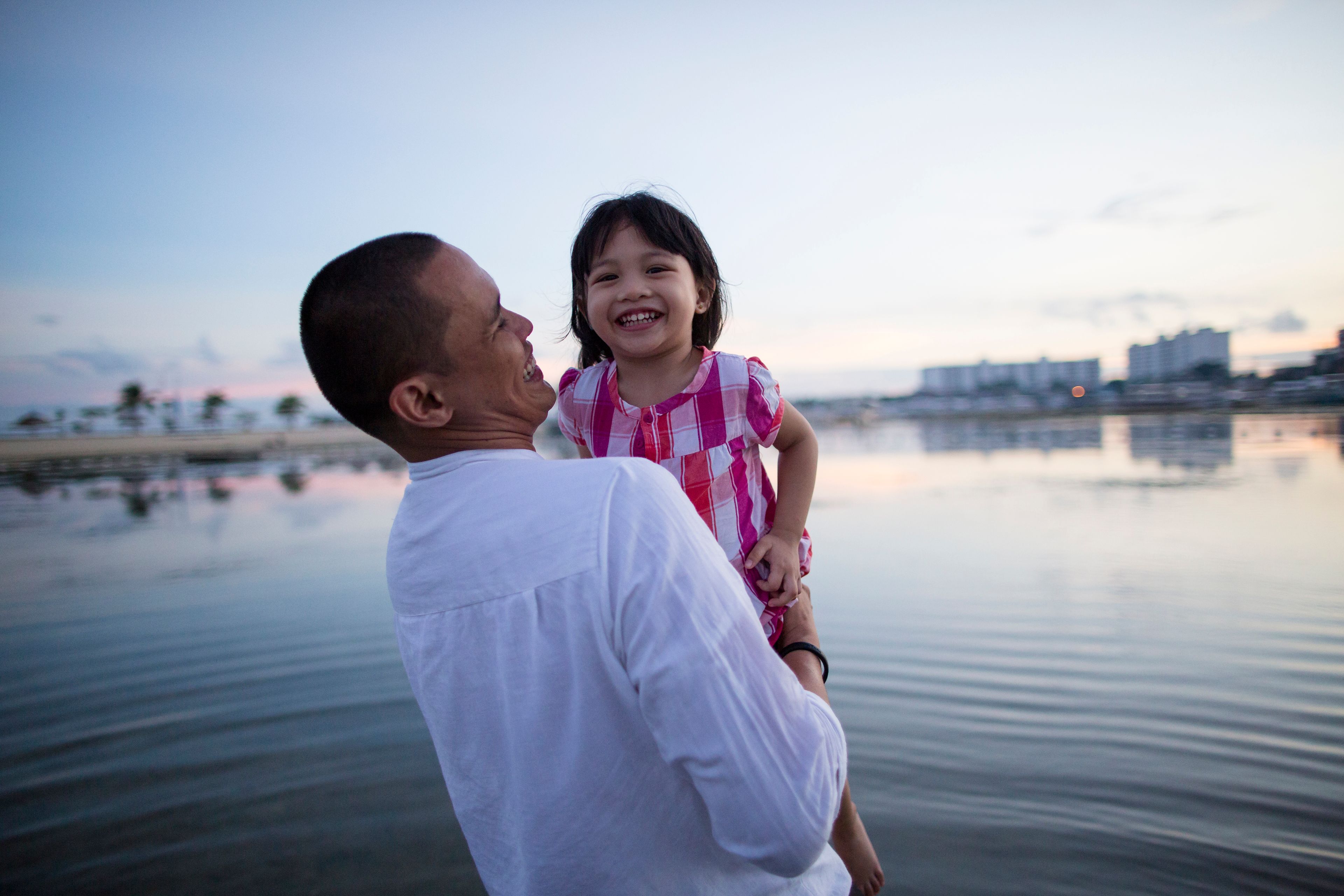 A father and daughter in the Philippines playing in the water at the beach.