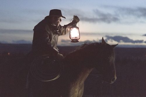 A man riding a horse at night holding a lantern