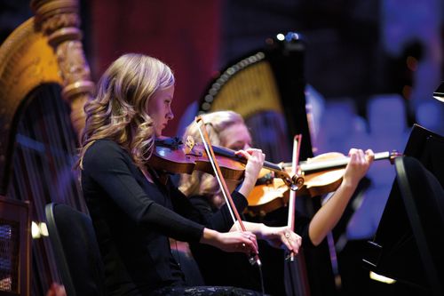 A woman with blonde hair and a black dress playing in the orchestra in the 2011 Christmas concert in the Conference Center.