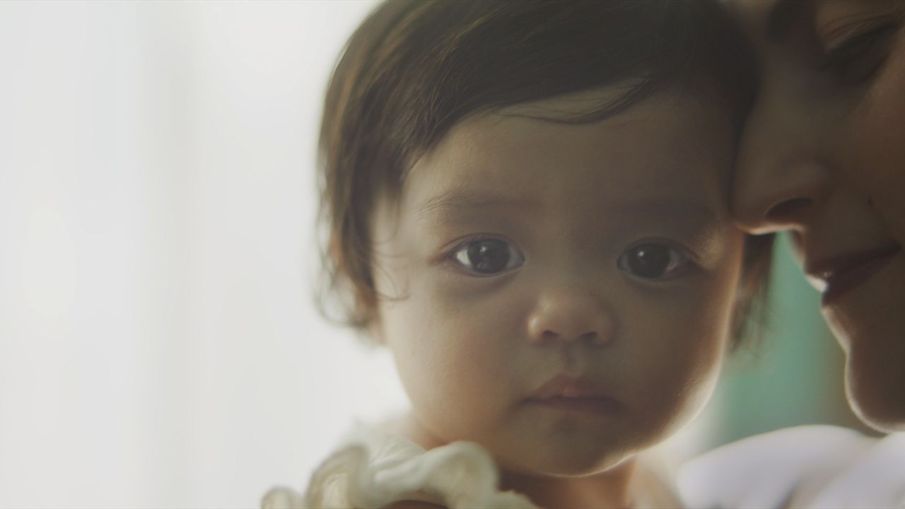 A baby girl looks forward while her mother holds her