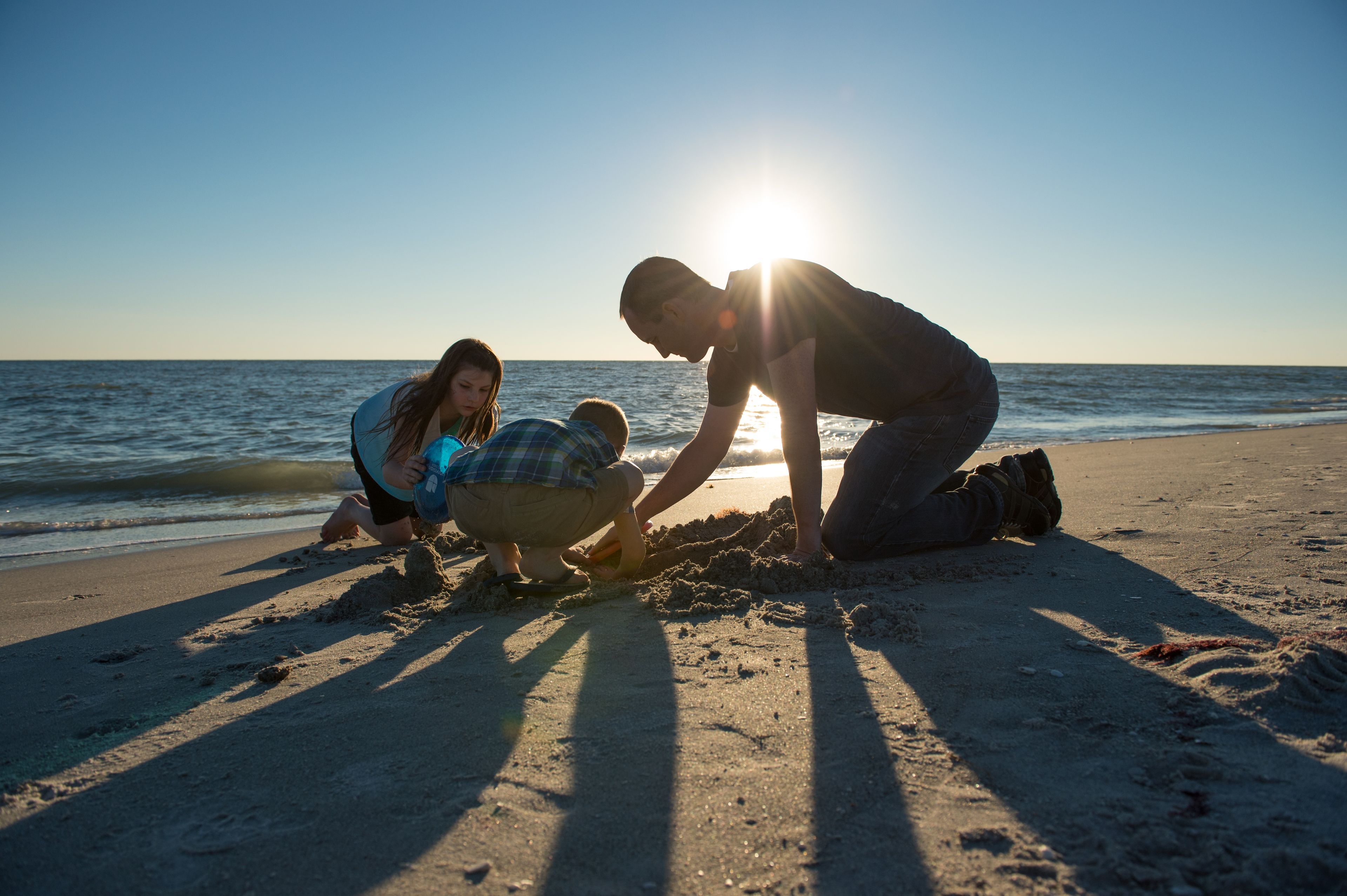 A father and his two children play in the sand on a beach together.