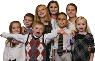 A group of Primary children.  A boy in front with his arms outstretched has Down's Syndrome.
