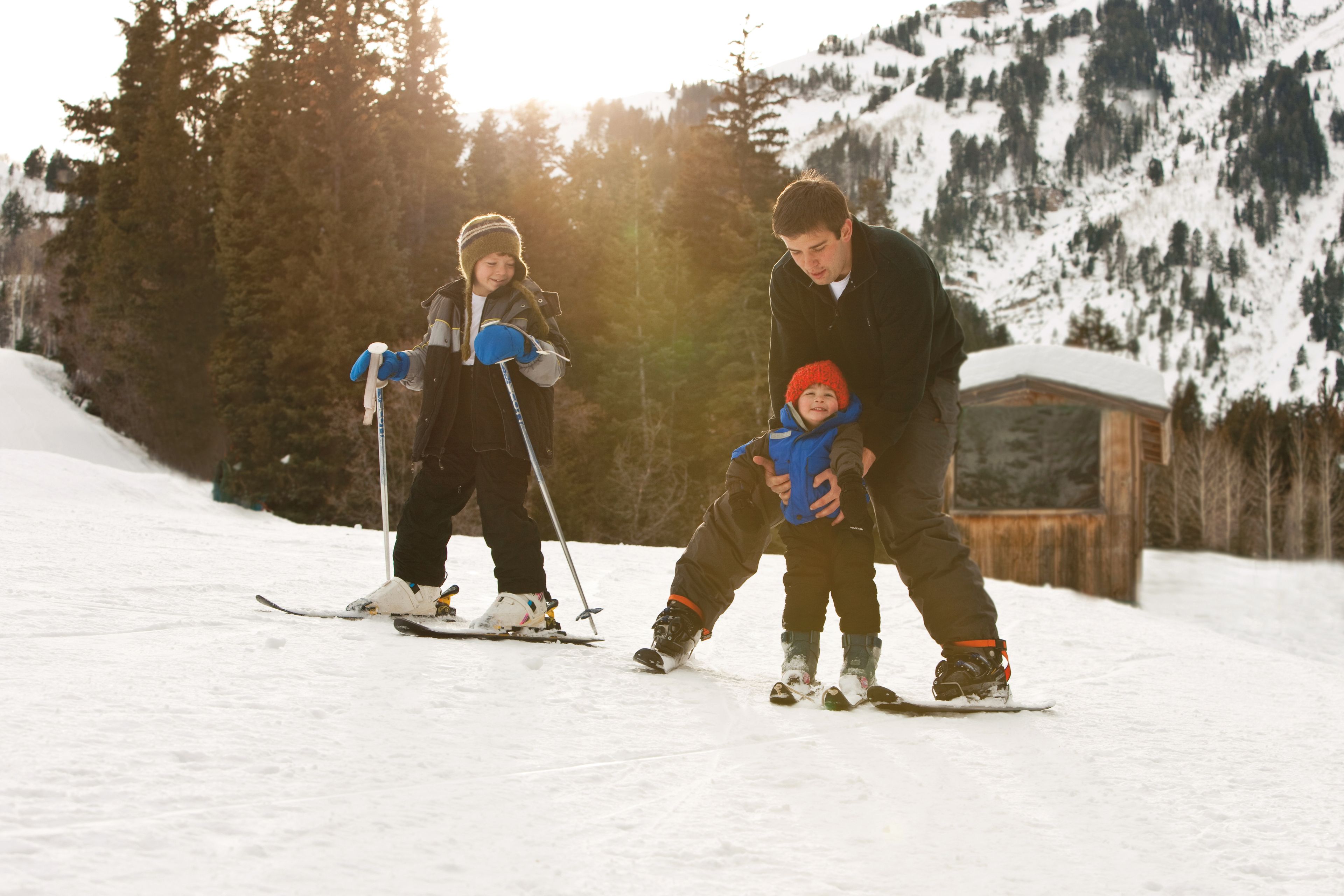 A father helps his two sons ski.