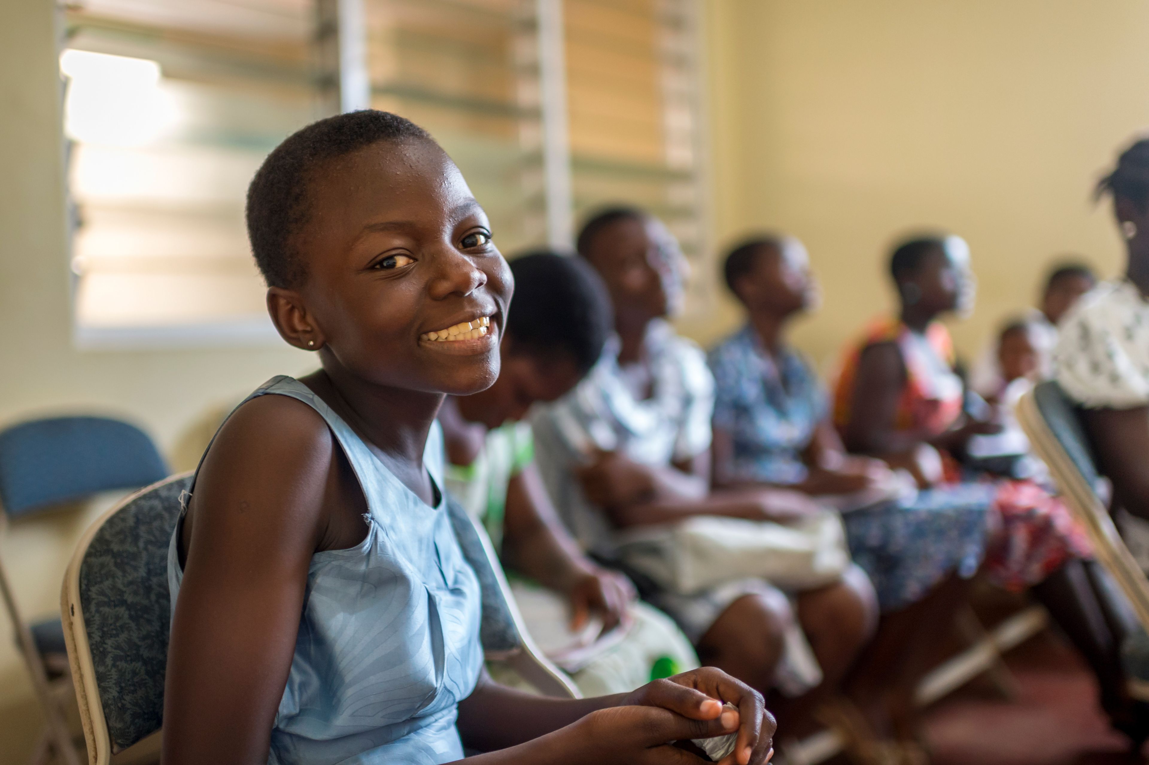 A young girl in Sunday School in Africa sits in a chair and smiles.