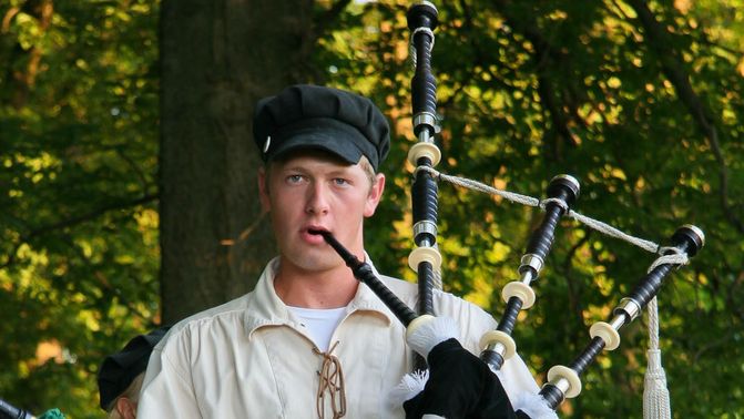 A young man in a kilt playing a bagpipe.