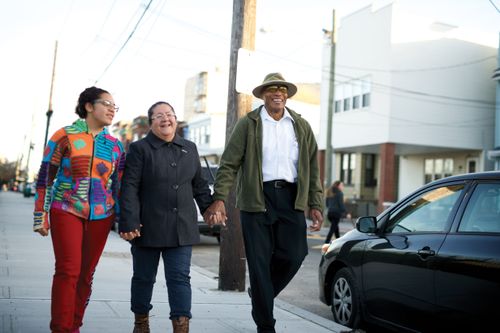 A couple walking hand in hand with their teenage granddaughter on a city street.