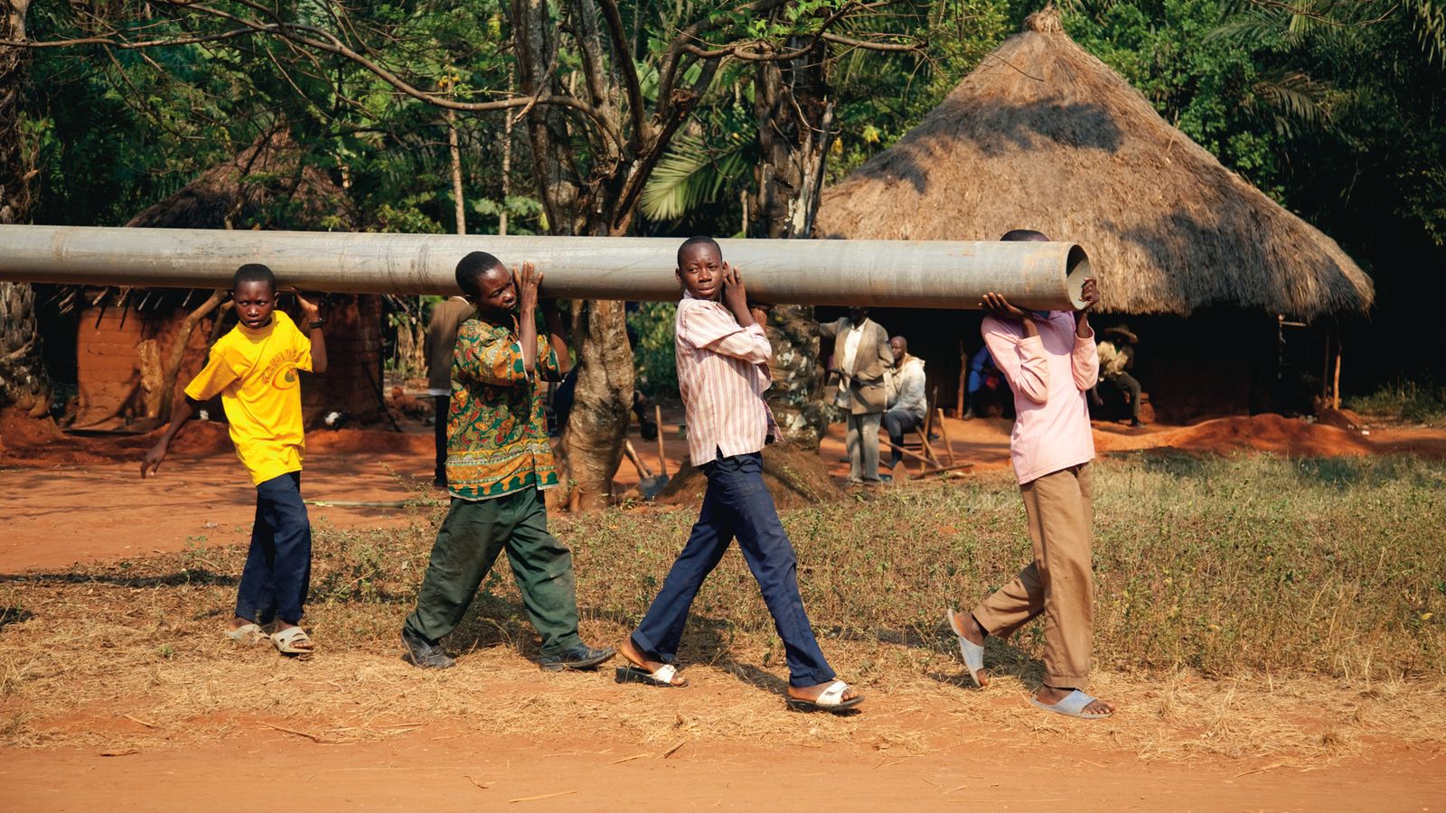 Four African boys walking and carrying a pole on their shoulders.