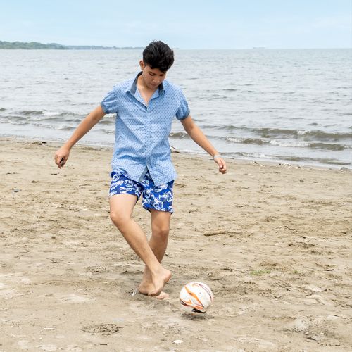 young man playing soccer on the beach