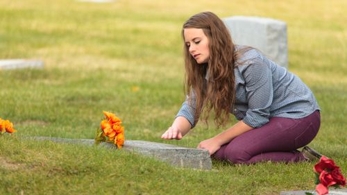 woman kneeling at cemetery headstone