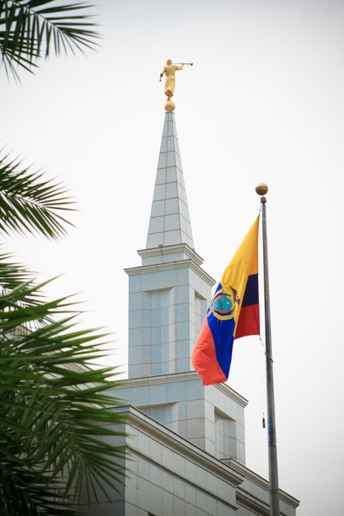 The spire of the Guayaquil Ecuador Temple, with palm leaves on the left side and the Ecuadorian flag on the right in the foreground.
