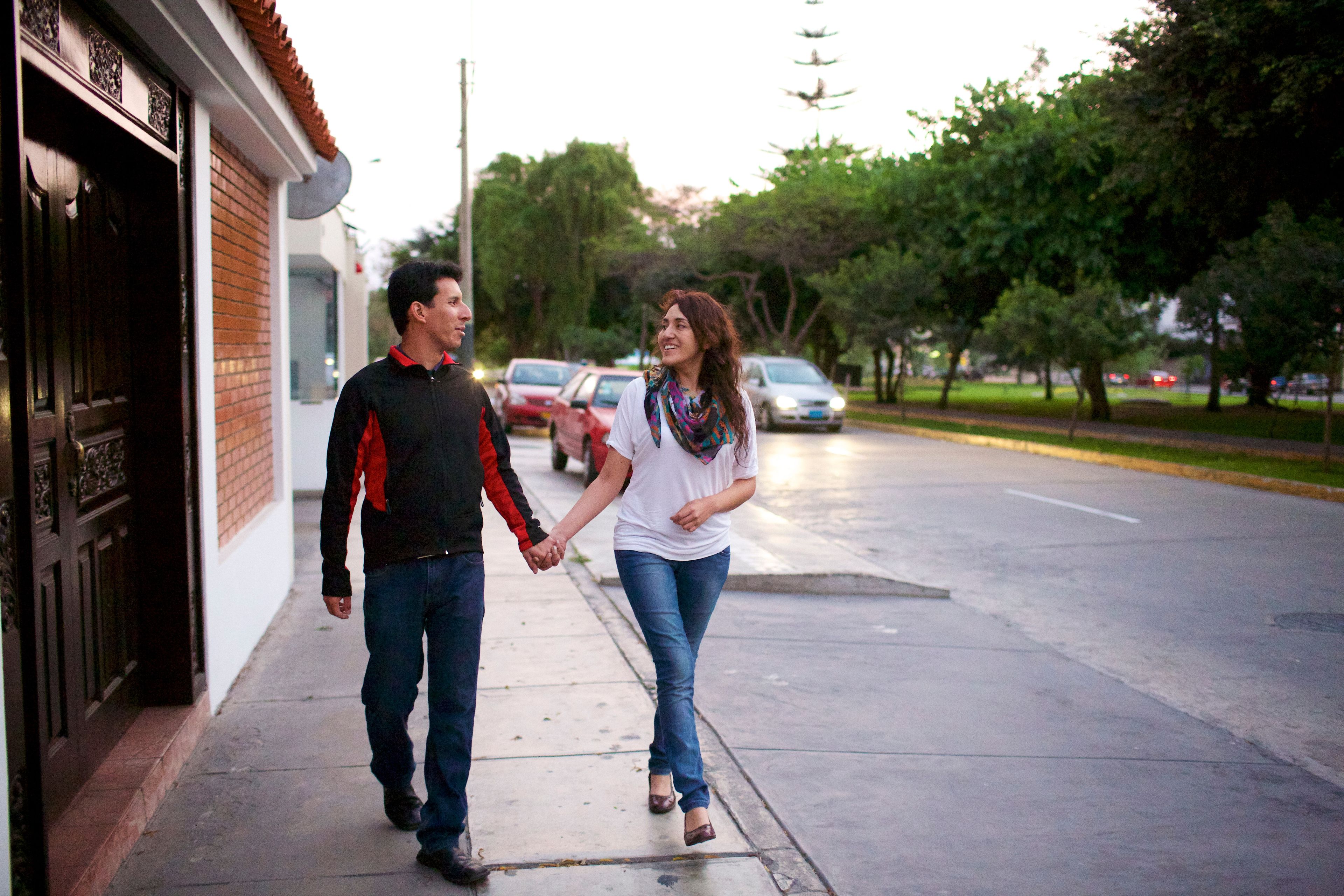 A husband and wife holding hands and walking down a sidewalk.