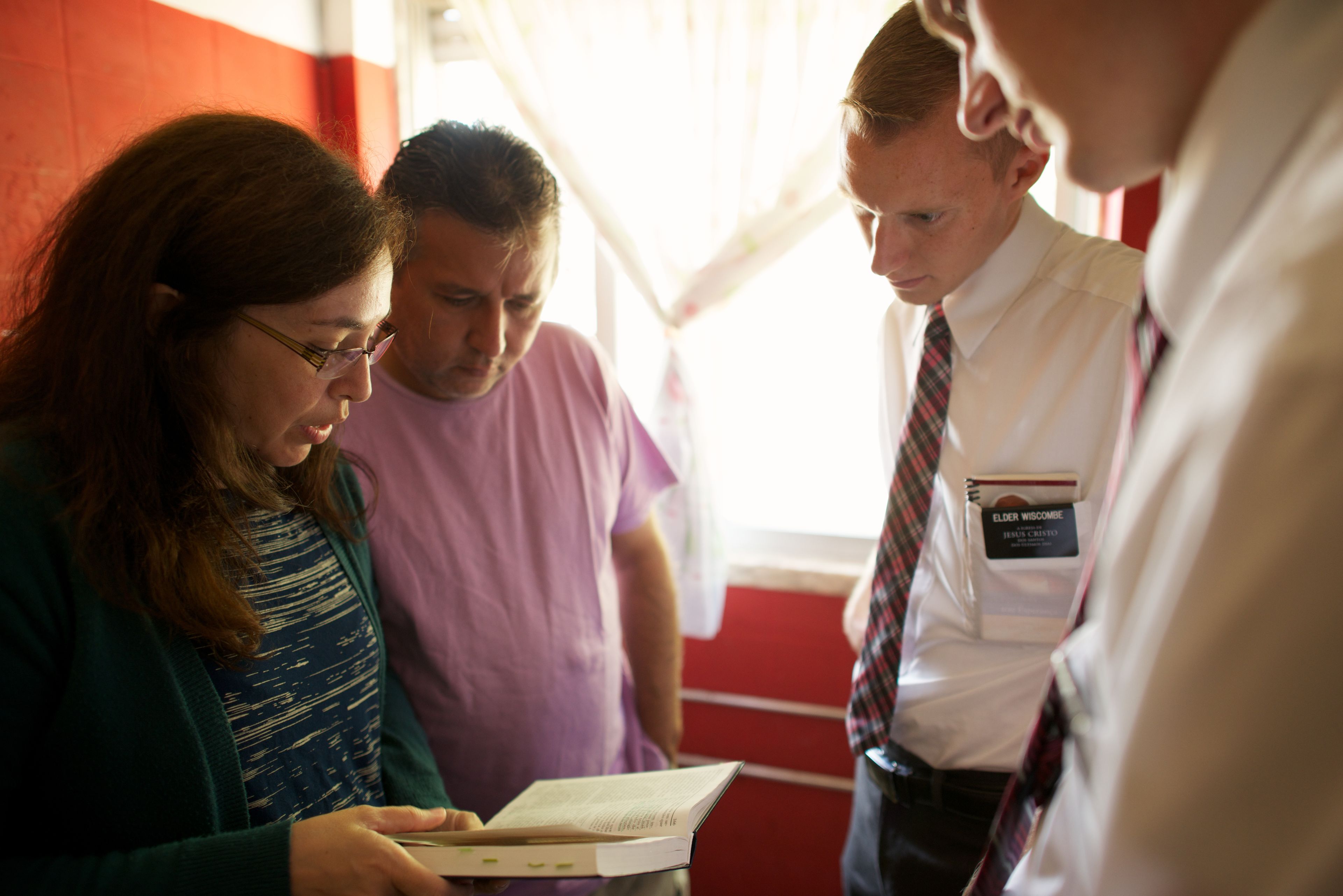 A couple standing with two elder missionaries and reading the scriptures.