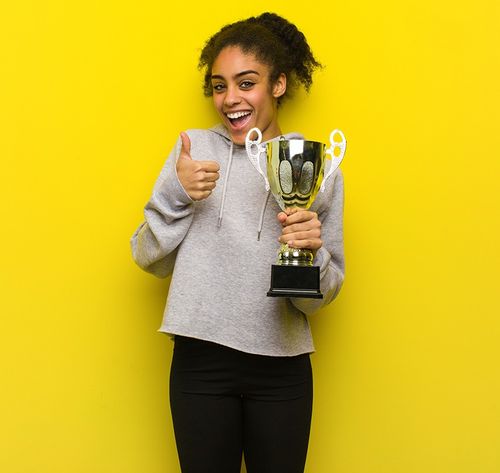 woman holding a trophy wearing a gray shirt and black pants