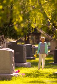 woman with flowers by headstones in cemetary