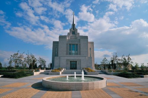 The fountain near the entrance to the Kyiv Ukraine Temple, with the temple in the background against the backdrop of a bright blue sky.