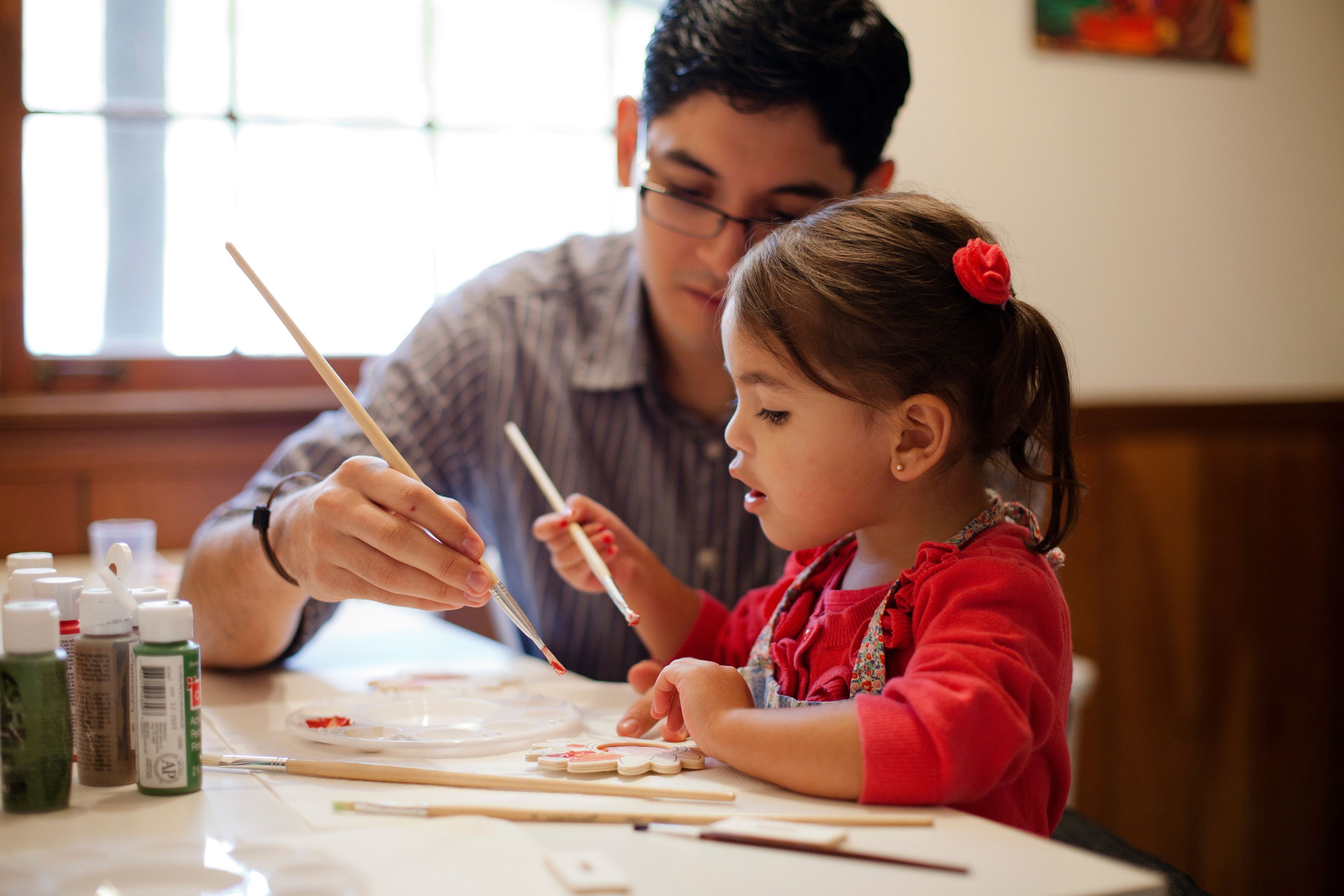 A toddler girl paints with her father.
