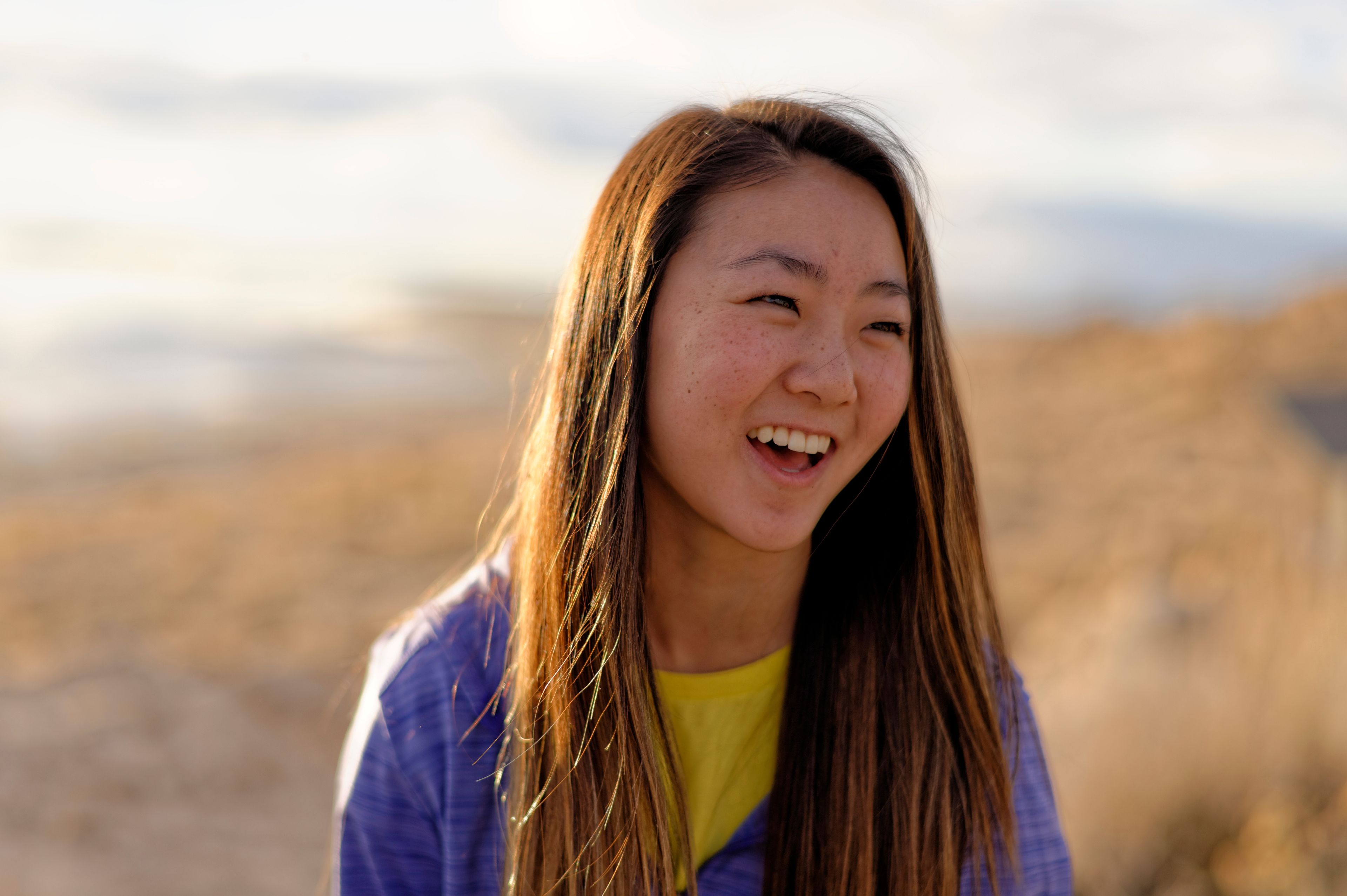 A portrait of a young woman outdoors, looking to the side and laughing.