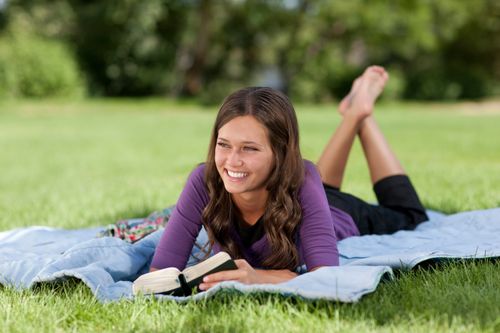 A young woman lying on the grass reading the scriptures and pondering.