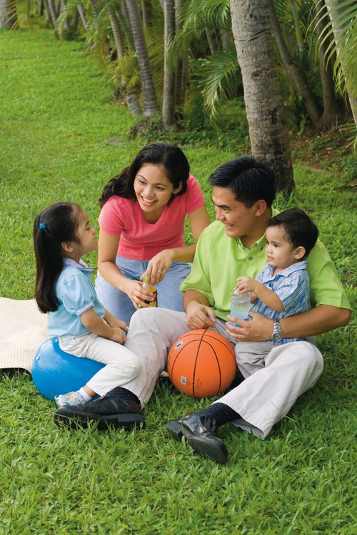 A father, mother, son, and daughter sitting outside on the grass with a basketball.