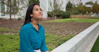 A woman sits outside the Mt. Timpanogos Utah Temple. She is reading the scriptures and is looking up towards the sky.