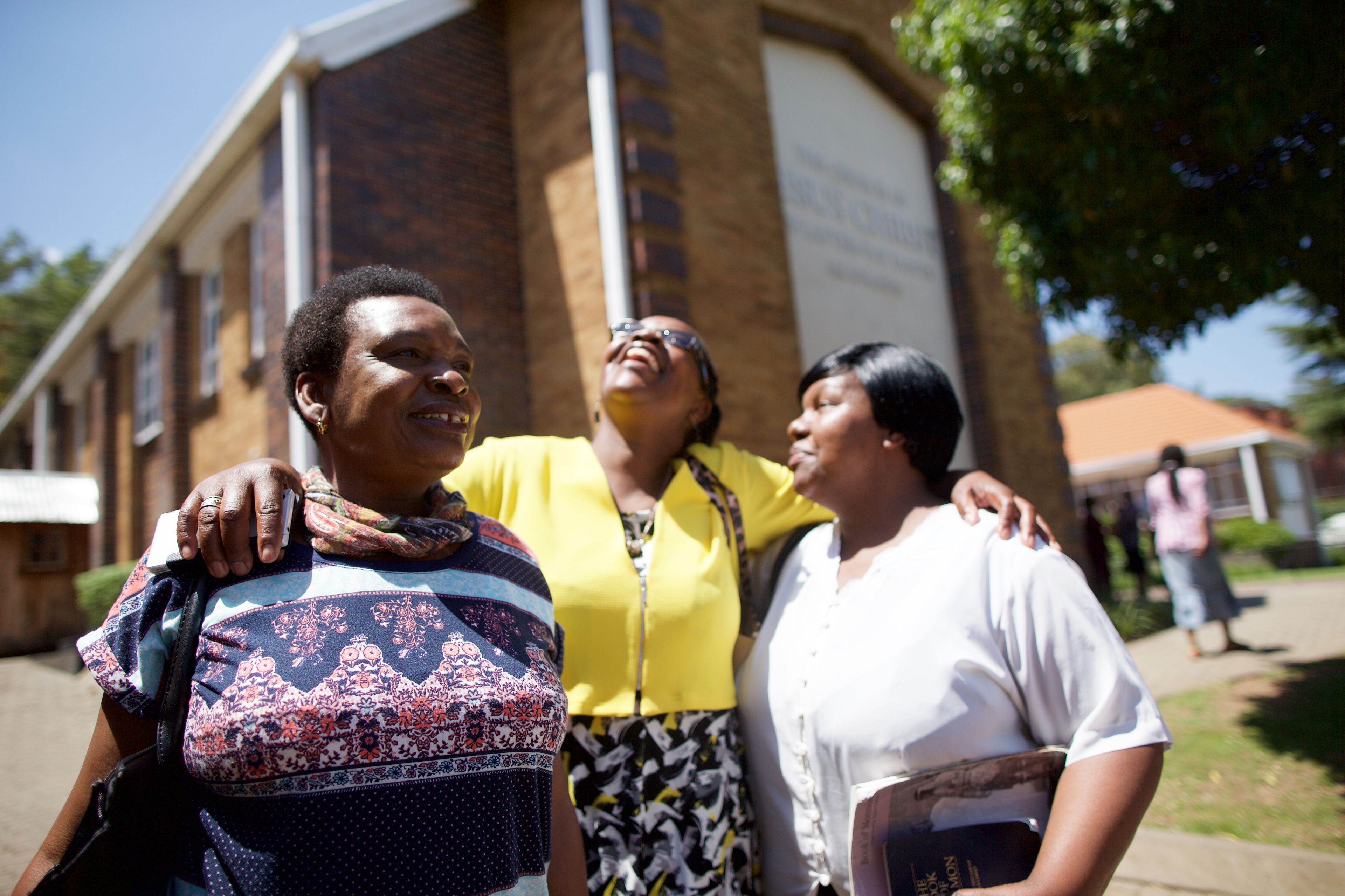 South Africa.  Members visiting after church on Sunday.  Three woman standing in front of the church.