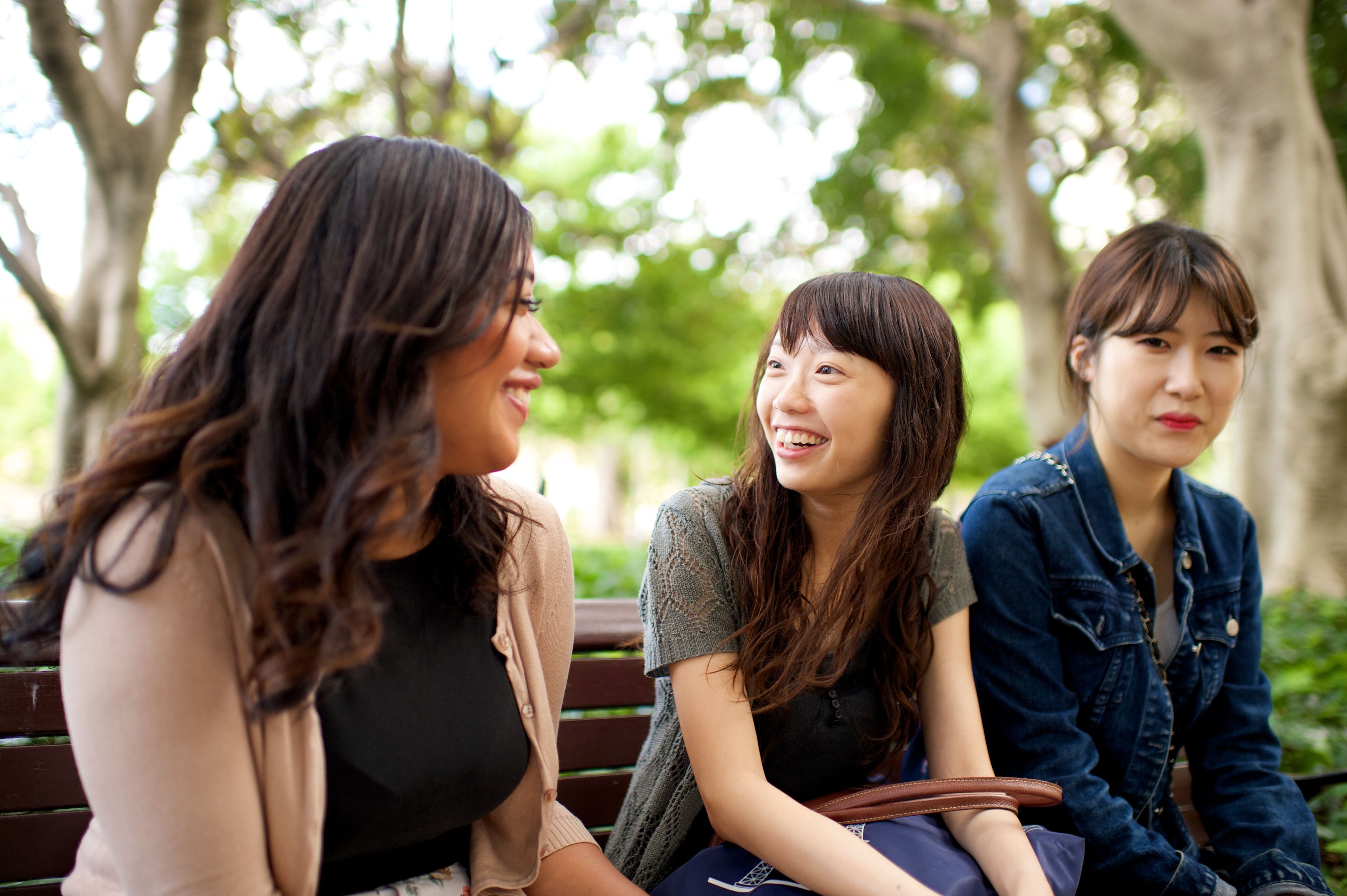 Three young women sit on a park bench together and talk.
