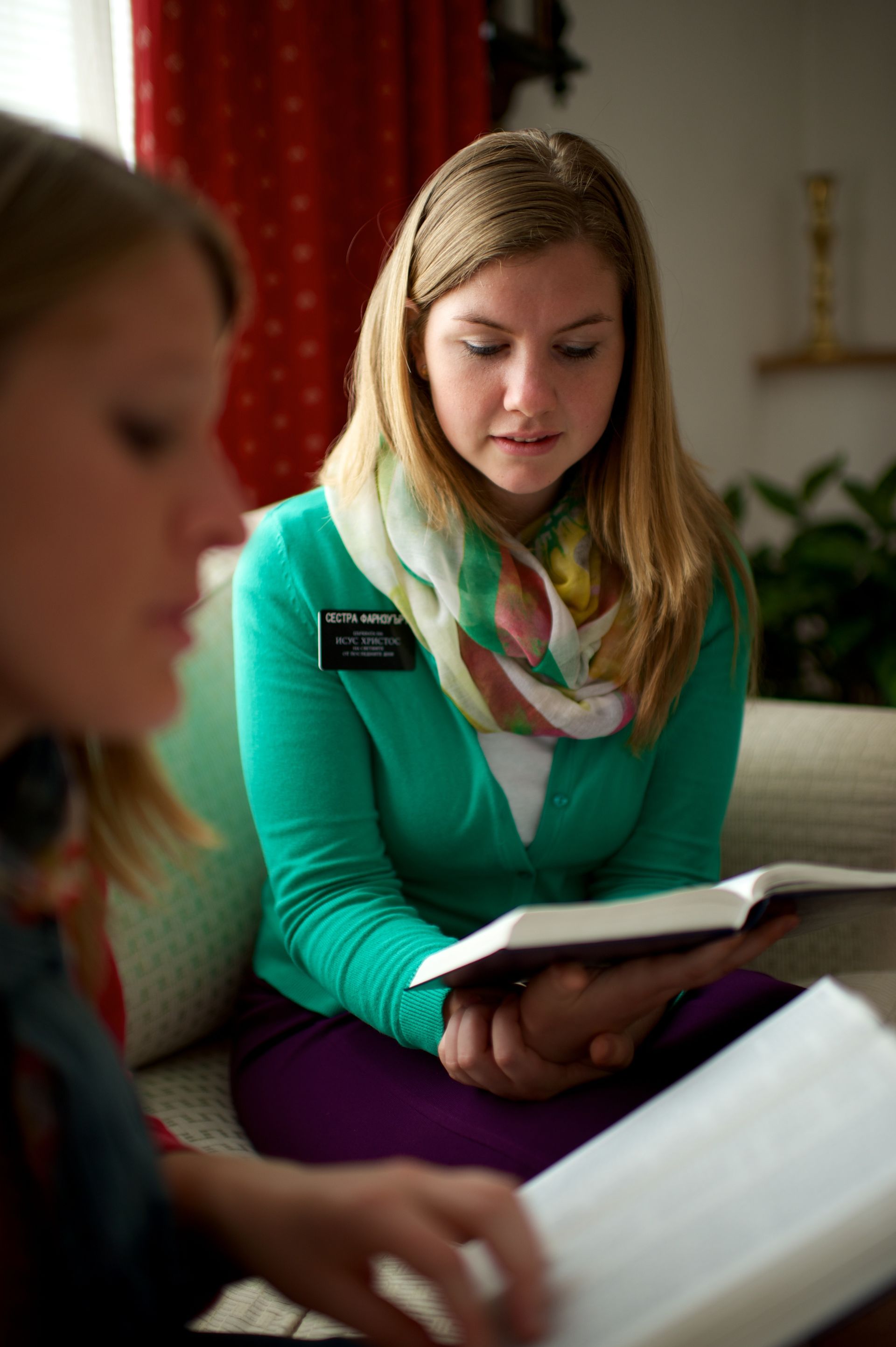 Two sister missionaries sit on a couch and read from their own scriptures.