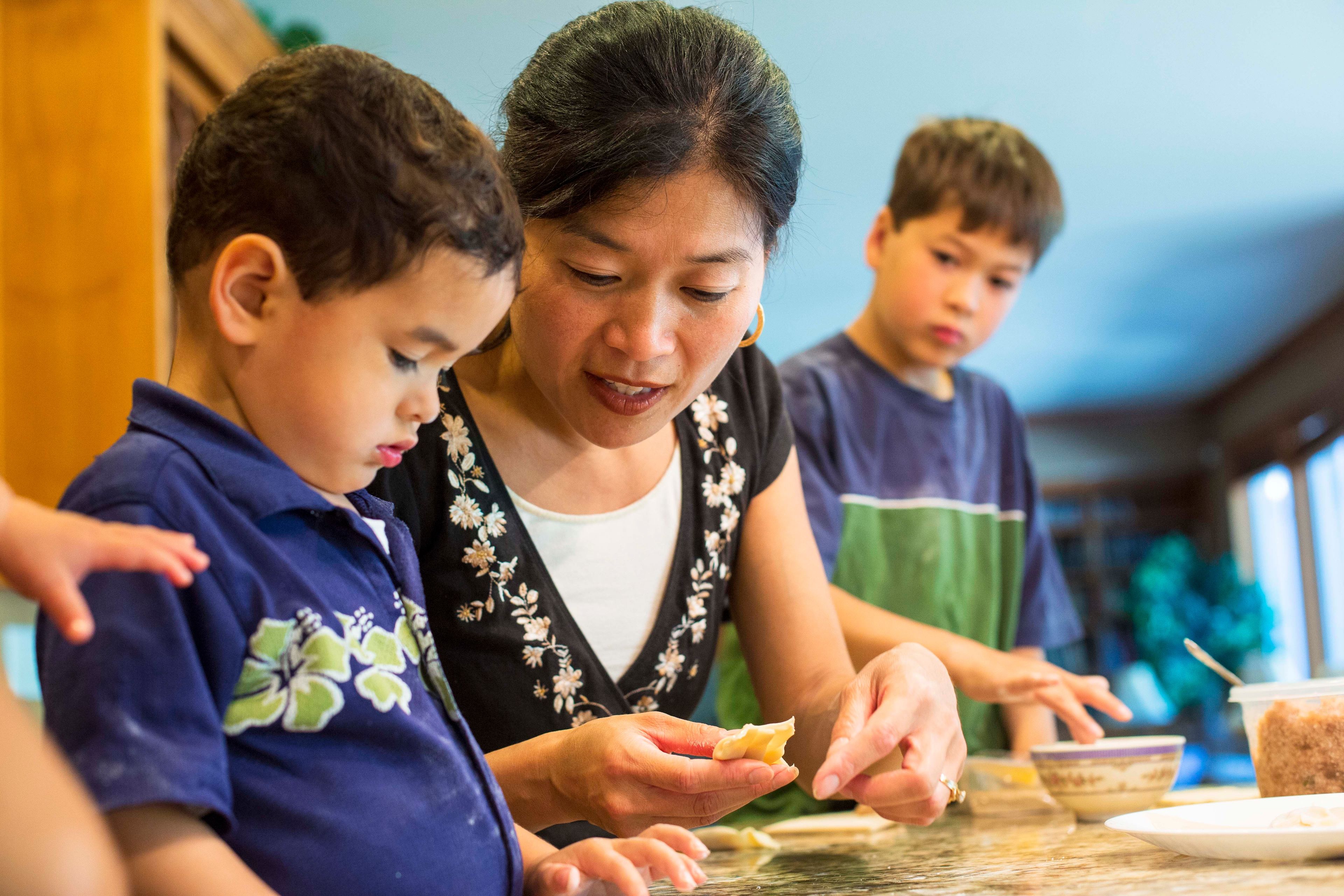 A mother and two of her sons preparing food together in the kitchen.