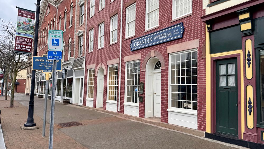 Red brick store front with blue sign reading “E.B. Grandin Printing Office and Book-Store"