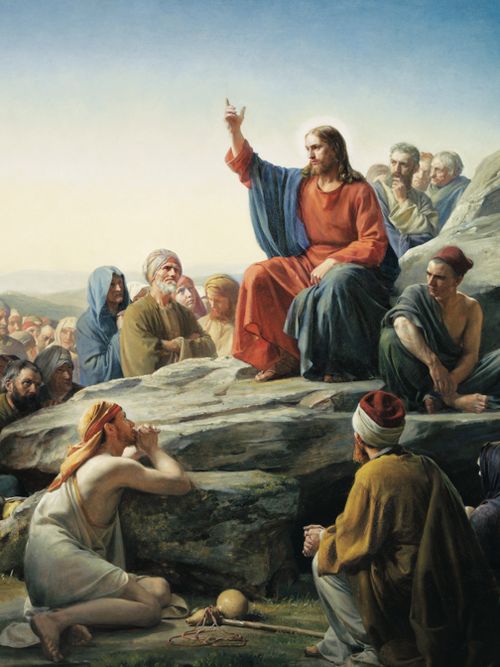Jesus Christ preaching to a multitude of people. Christ is seated on a rocky hillside. He is dressed in red and blue robes. He has one arm raised. Some of the figures have their hands clasped in devotion.