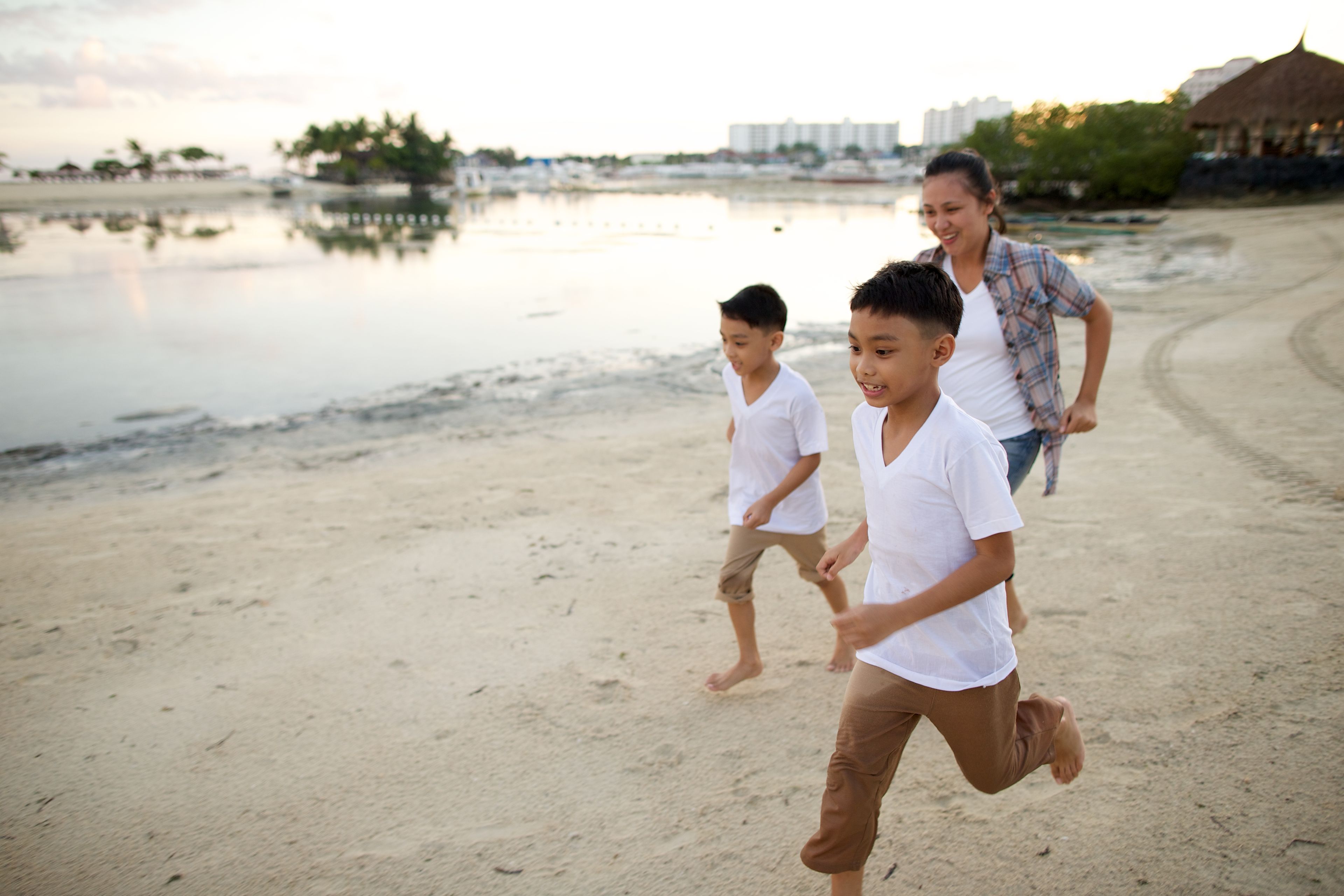 Two young boys run with their mother on a beach.