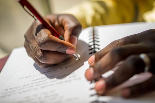 Hands of an African American person writing in a notebook.