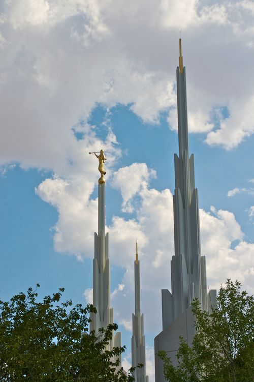Three spires on the Las Vegas Nevada Temple, with the angel Moroni statue, seen above the green leaves of nearby trees in the daytime.