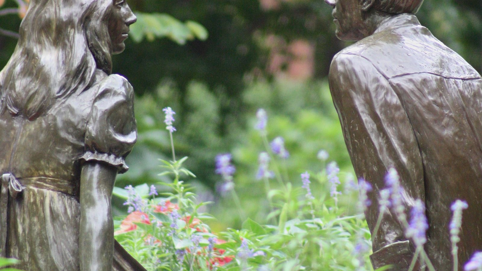 A male and female bronze statue sitting across from each other in a garden.