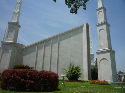 A front partial view of the Lima Peru Temple, showing some of the green lawns and large bushes on the grounds and several of the temple’s spires.