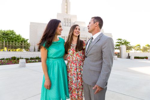 A teenage girl with brown hair standing between her parents in front of the Draper Utah Temple.