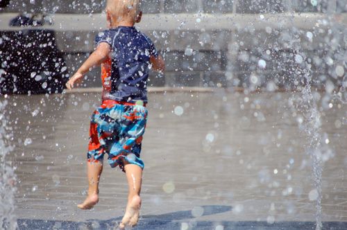 A little boy runs around on a splash pad.