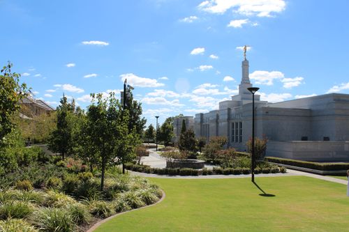 A view of the Perth Australia Temple from some distance back on the temple grounds, showing green trees growing to the left.
