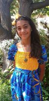 A young Polynesian or Hawaiian girl with long dark hair smiles. She has trees behind her.