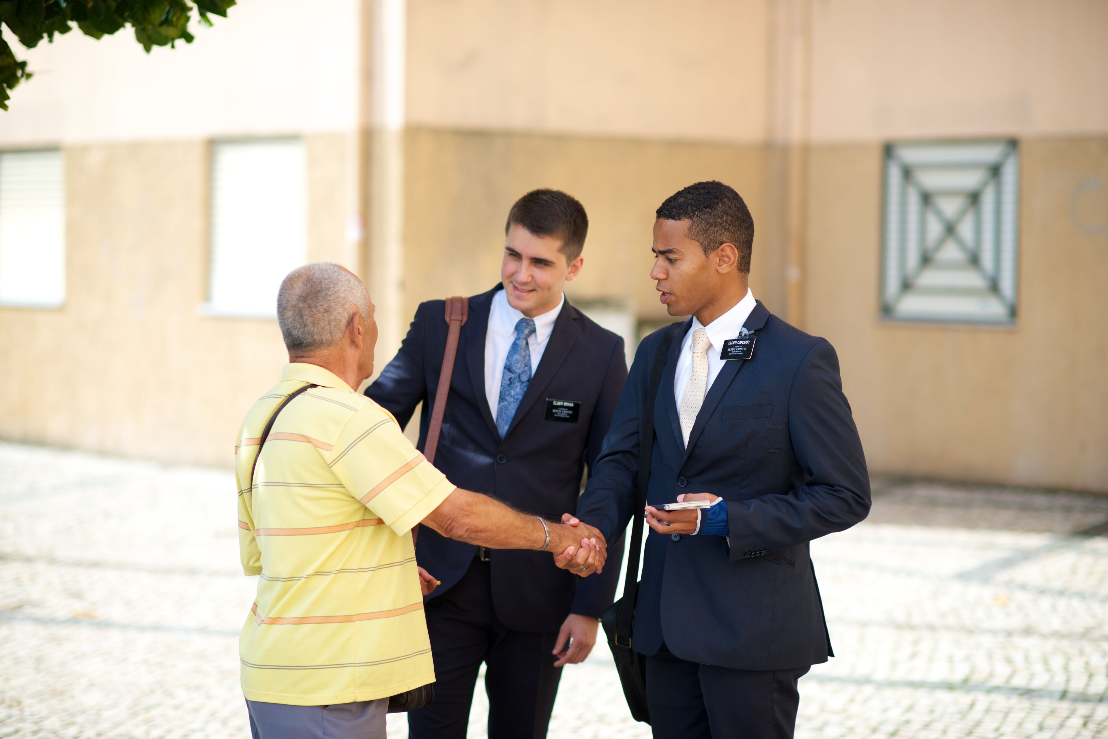 A man shaking hands with two elder missionaries in the street.