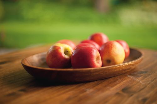 Red apples in a wooden bowl on a table outside.