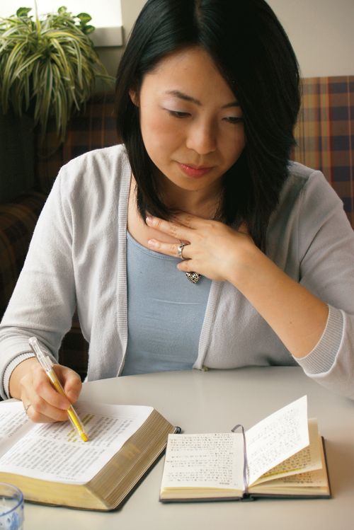 A Chinese woman sitting at a table with scriptures open in front of her.  She is using a highlighter to mark them.