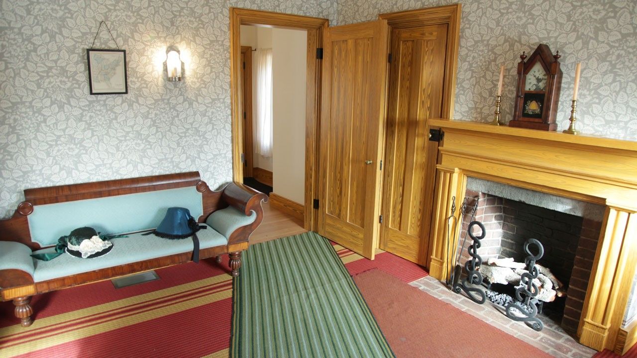 Carpeted and wallpapered room with a couch, doorway, and fireplace. 